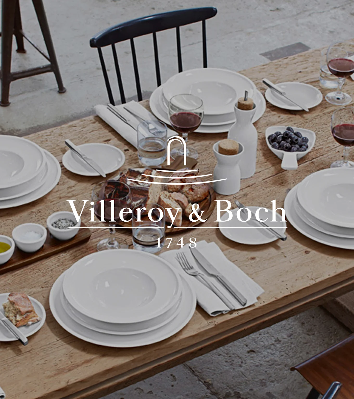 Ett rustikt träbord dukat med Villeroy & Boch vitt porslin, vin, bröd, blåbär, salt, peppar och olivolja för en måltid.