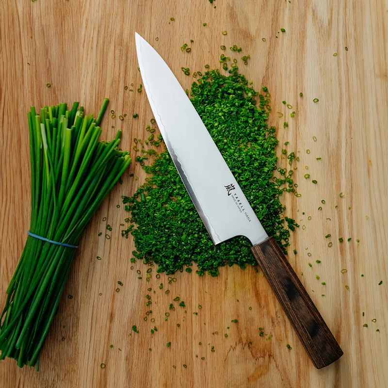 En kockkniv ligger på en träskärbräda med hackad gräslök och en bunt färsk gräslök.