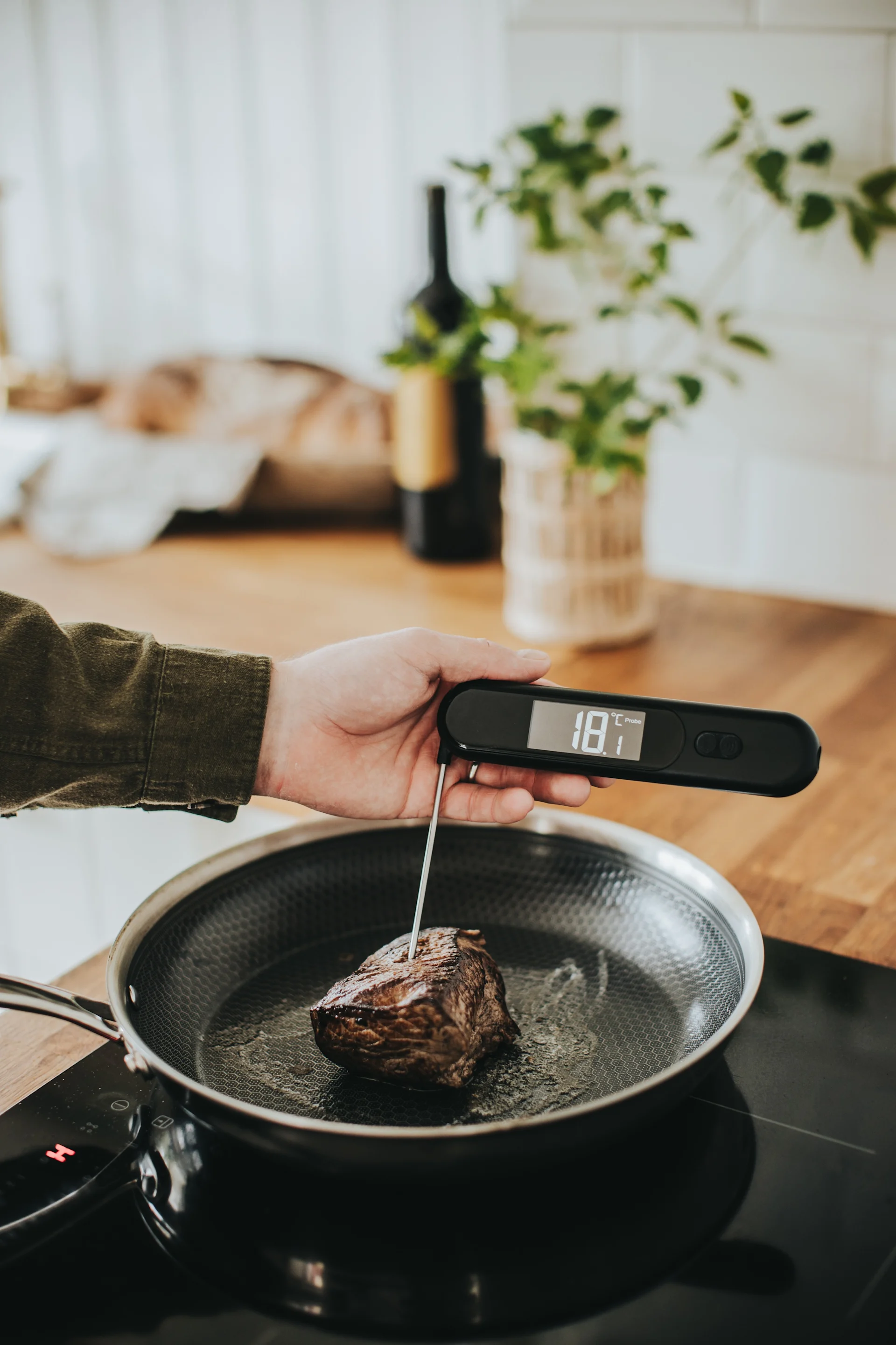 Hand kontrollerar köttemperatur med en digital termometer i en stekpanna.