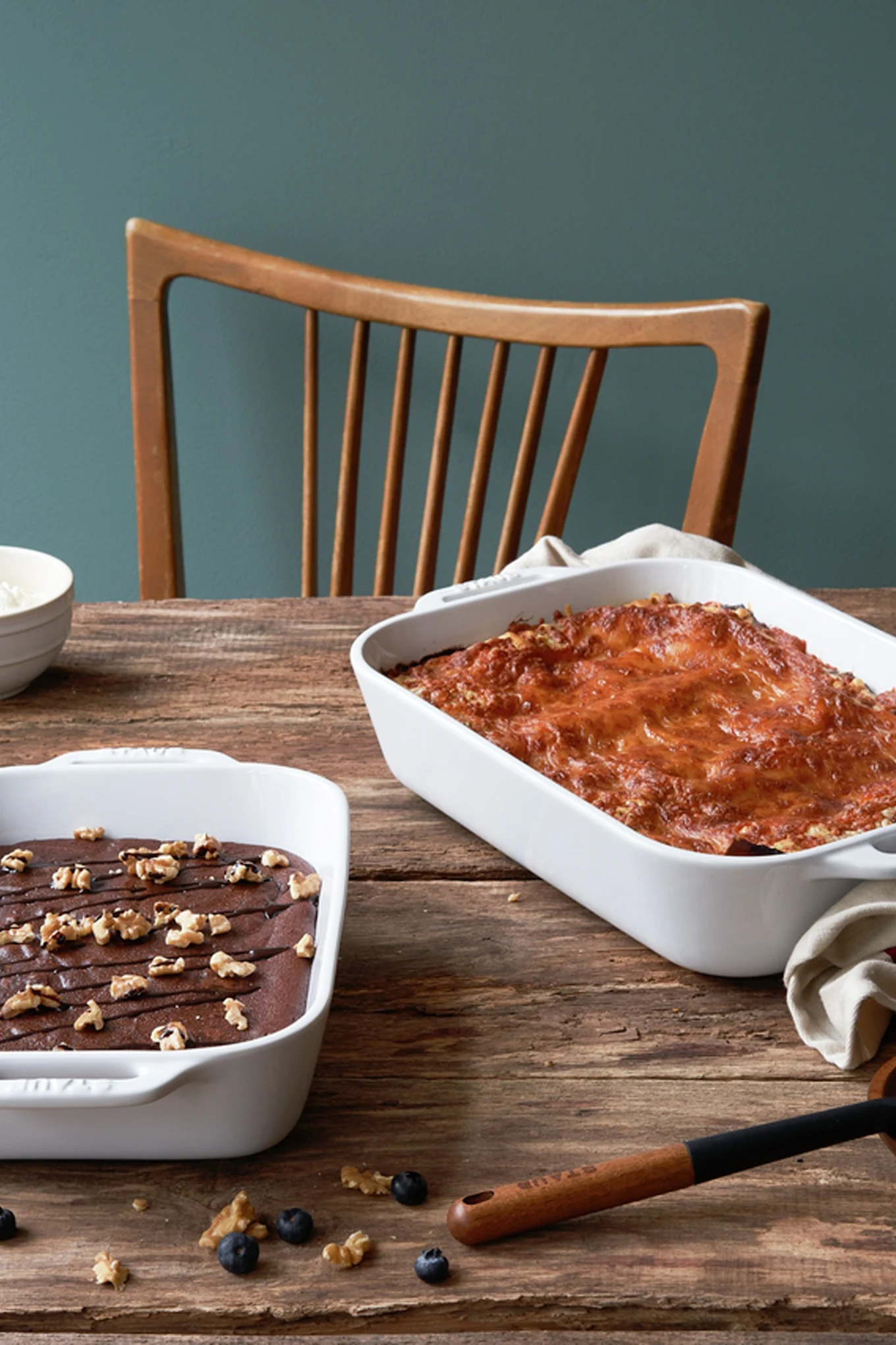 Två Staub-grytor, en mindre med chokladkaka och en större med lasagne, står på ett träbord.