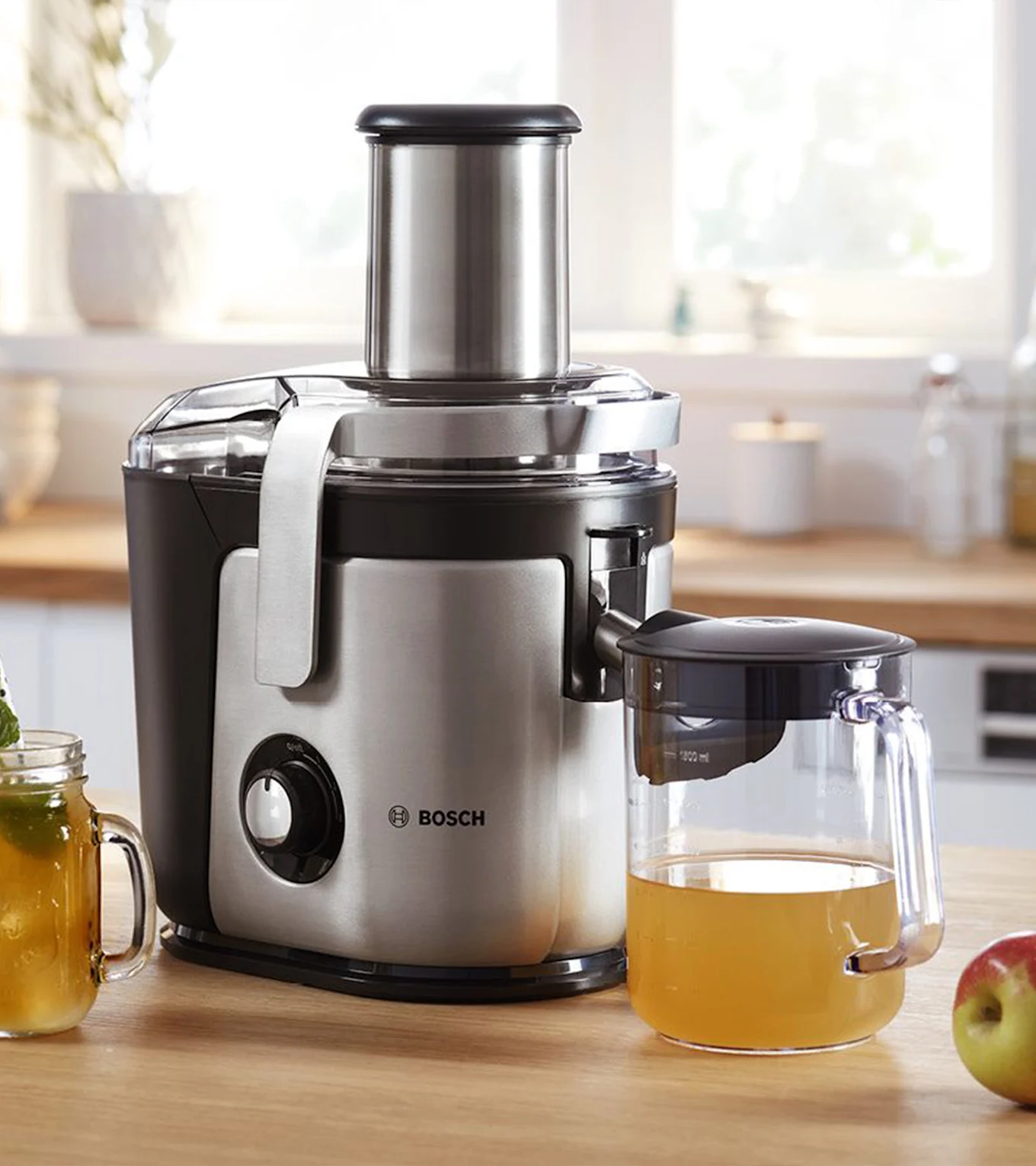 Bosch råsaftcentrifug, silver och svart, på en köksbänk med en kanna äppeljuice och ett äpple.