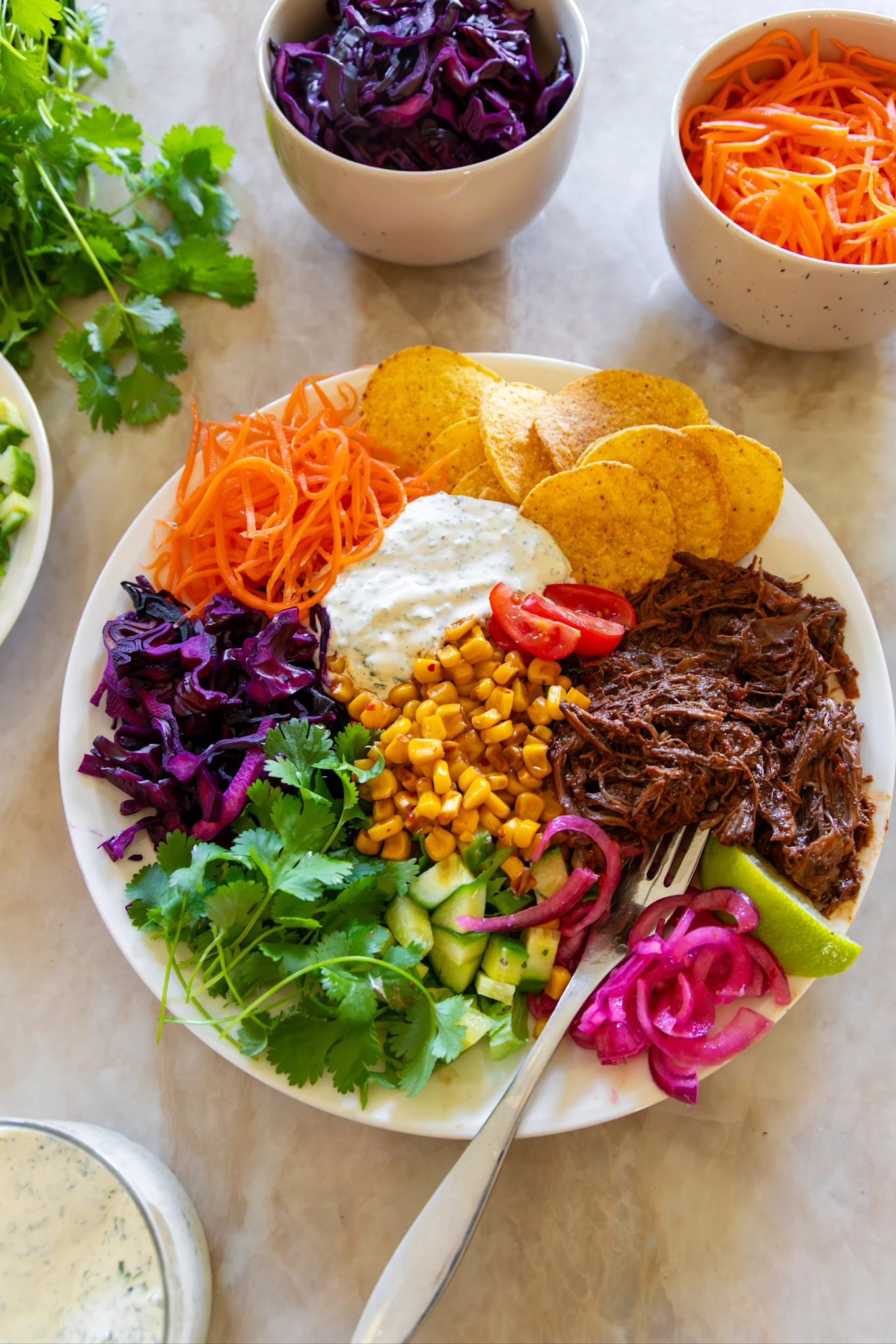 En färgrik taco bowl med pulled kött, majs, inlagd lök, morötter, kål, koriander, gurka, tomater, tortillachips och sås.