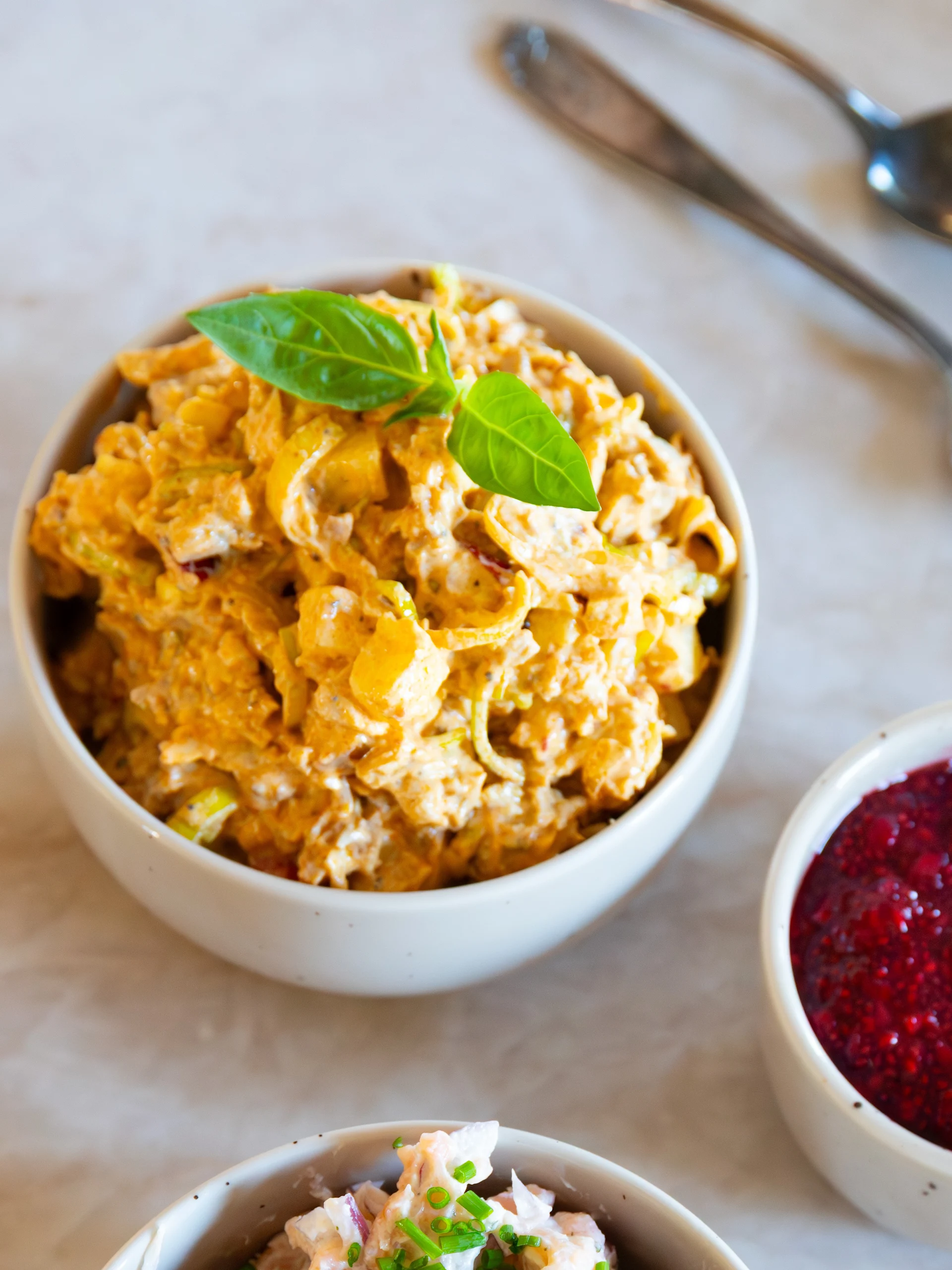 Tre skålar på en ljus yta: krämig orange sallad med basilika, röd sylt med en sked och krämig rosa sallad med gräslök.