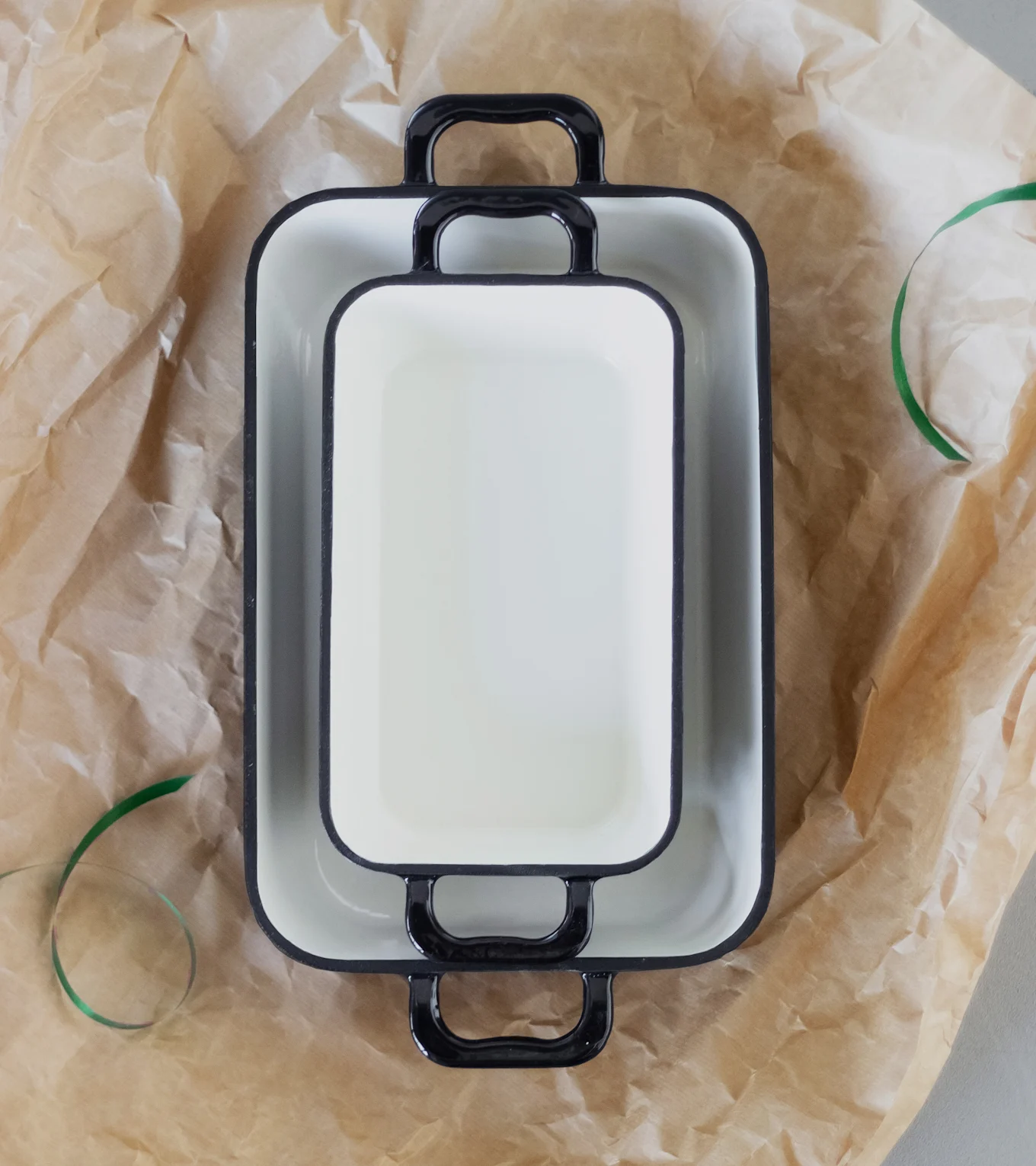 Två vita ugnsformar med svarta handtag, staplade på brunt papper.