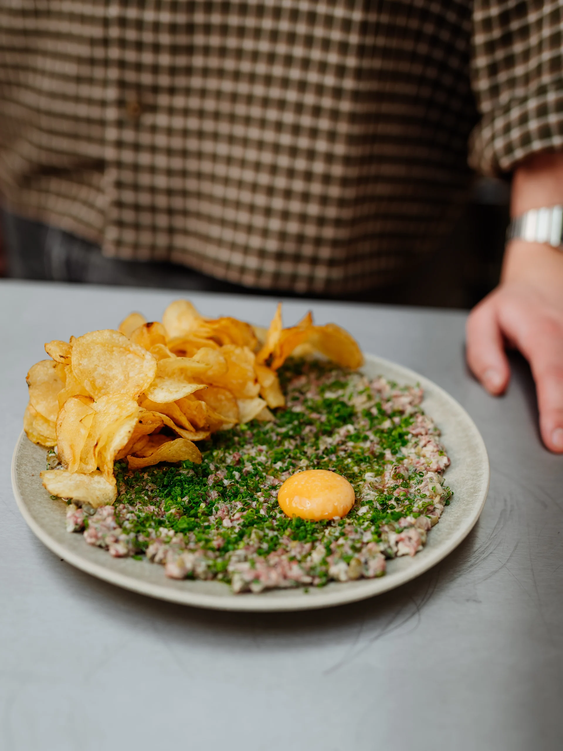 Biff tartar med en rå äggula, gräslök och en sida av potatischips på en tallrik.