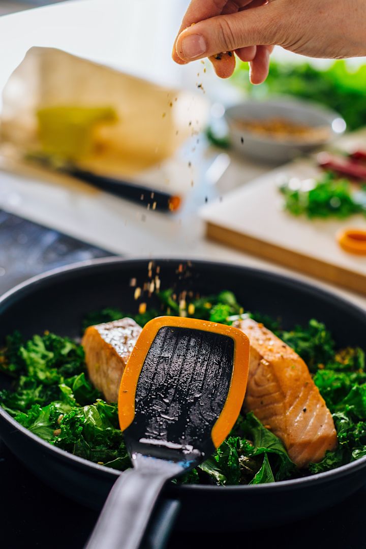 Functional Form-spateln från Fiskars placeras på en stekpanna med fisk och spenat i.