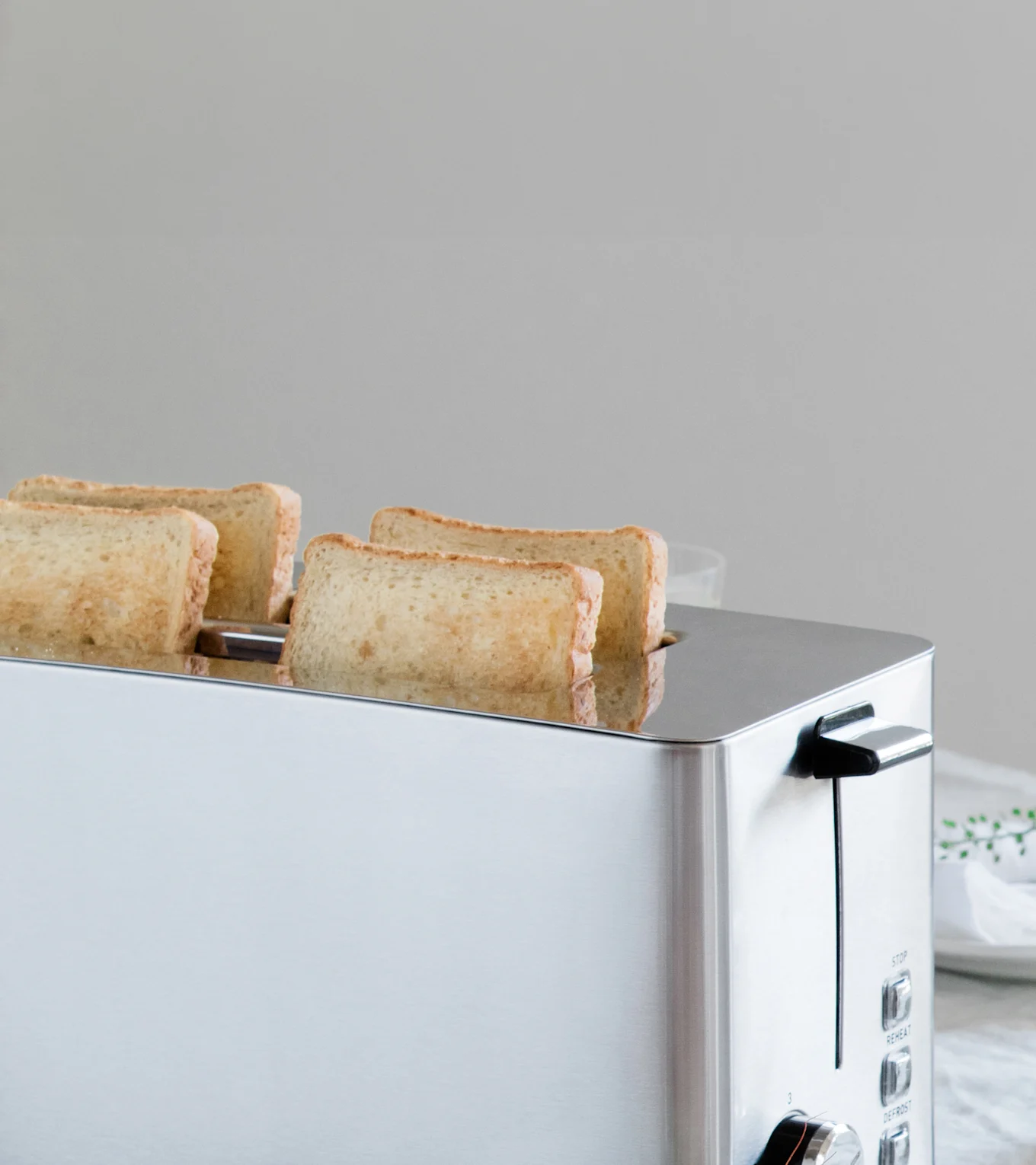 En silverfärgad brödrost med fyra skivor lätt rostat bröd som delvis stigit upp ur dess springor.