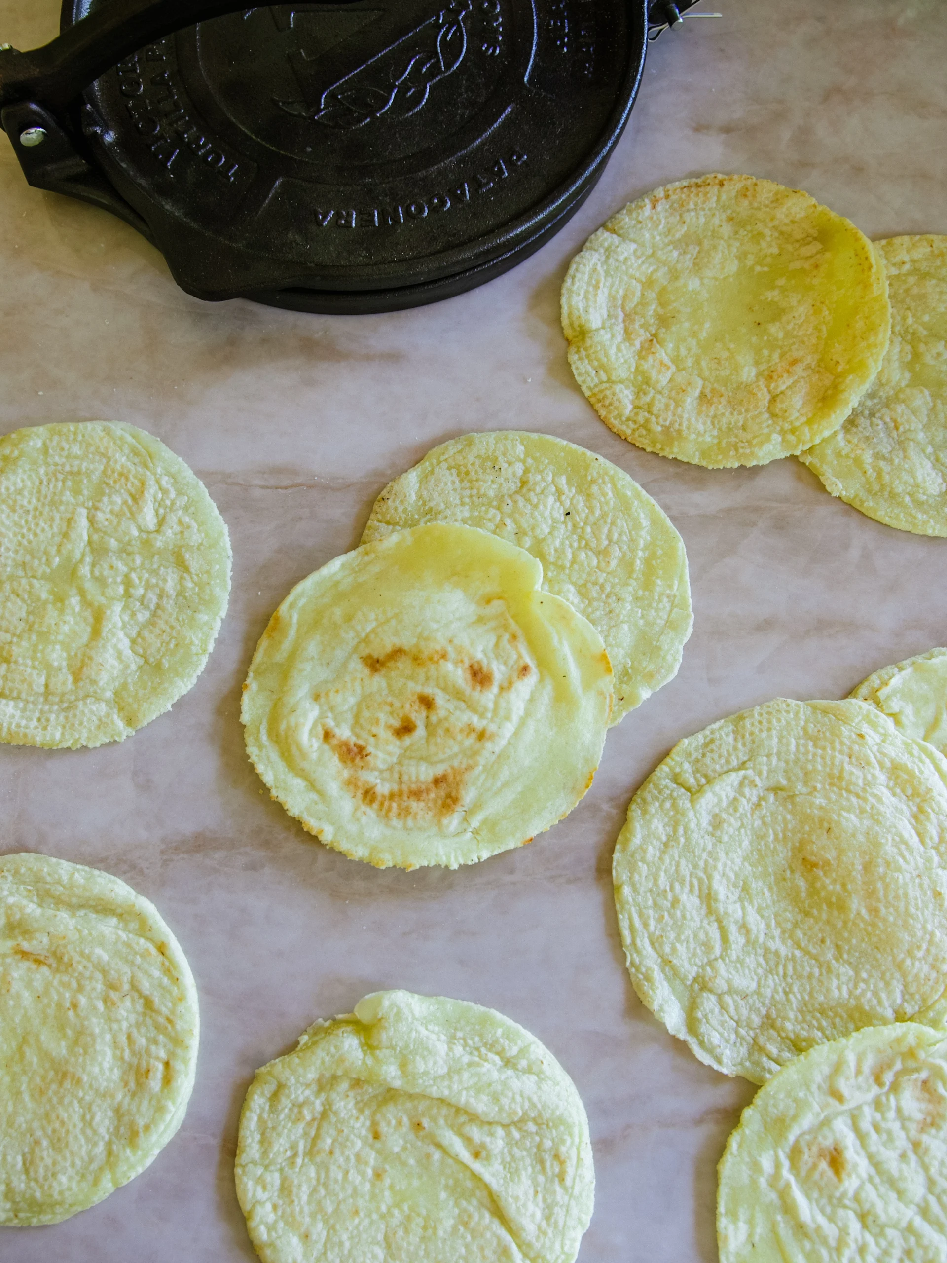 Nypressade gula majstortillas med en svart tortillapress i bakgrunden.