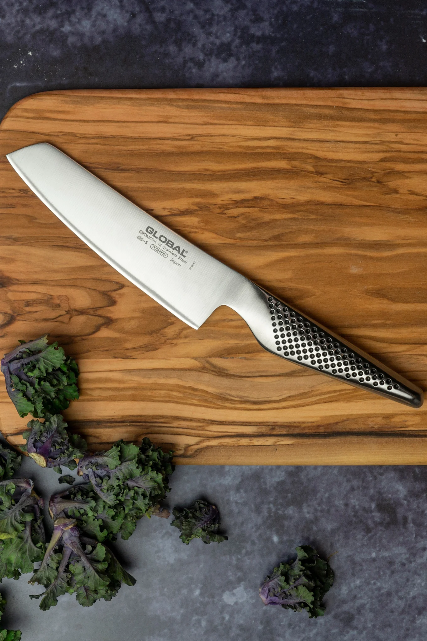 Global GS-5 grönsakskniv som tillhör Global knivserien Classic, ligger på en skärbräda. 