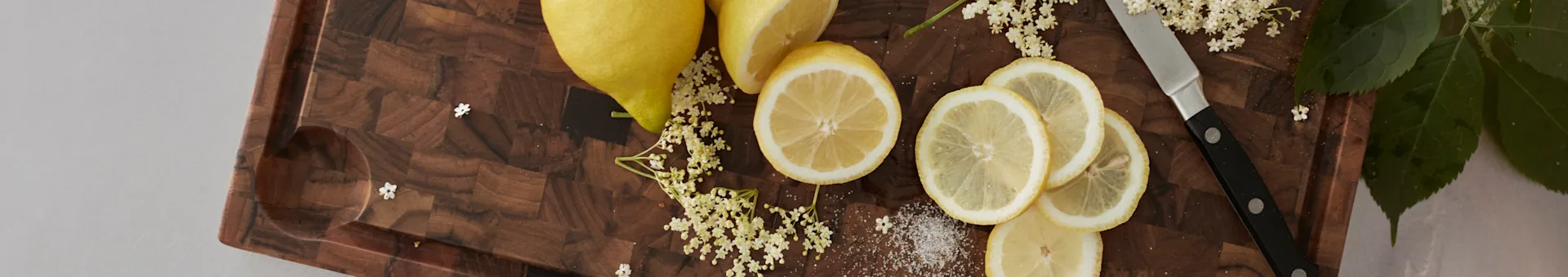 Citroner, fläderblommor och socker på en träskärbräda med en kniv.