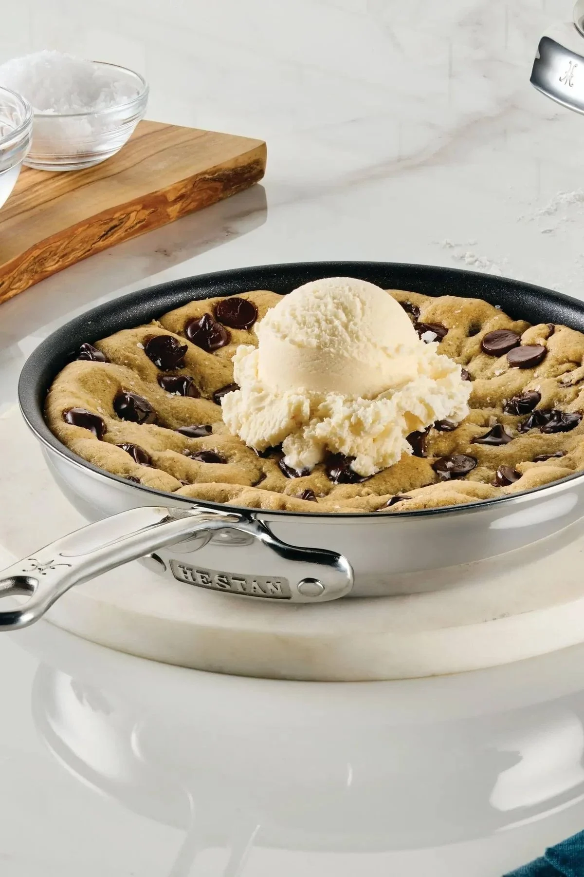 En Skillet-cookie med vaniljglass, chokladbitar och saltflingor, med bakingredienser i närheten.