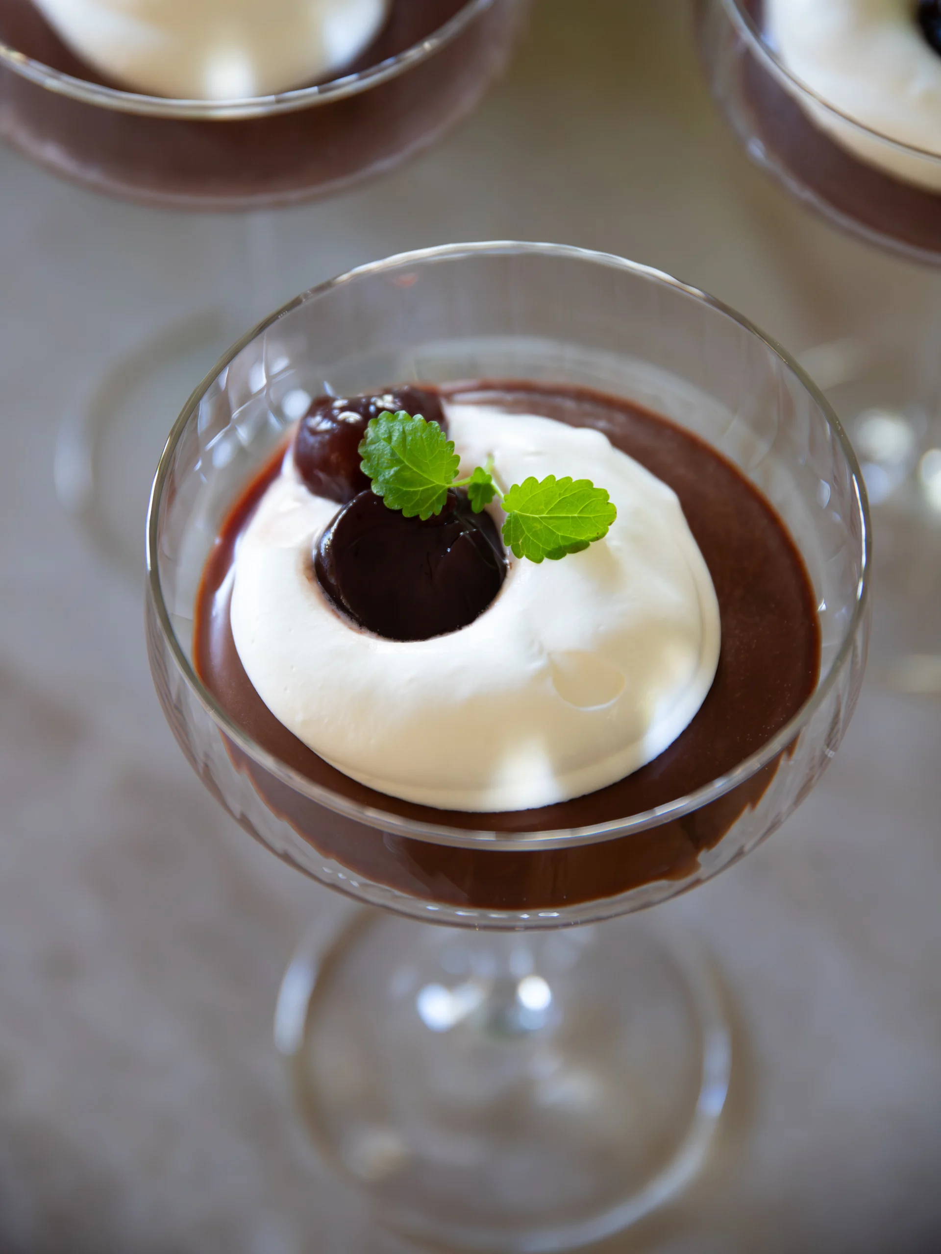 Chokladpudding med vispad grädde, körsbär och mynta i glas.