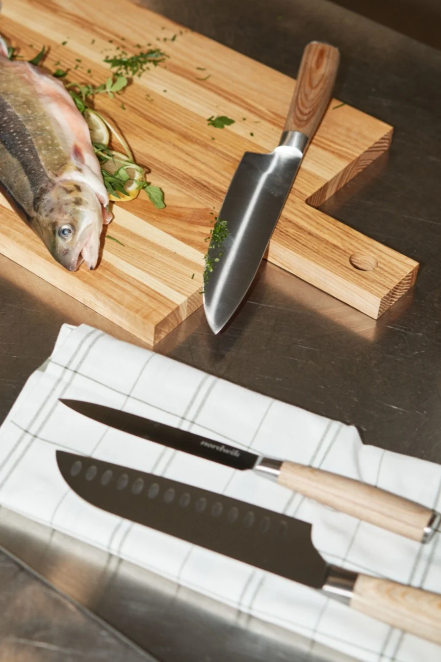 Färsk fisk, citron och örter på en skärbräda med en kniv. Två andra knivar vilar på en vit handduk.