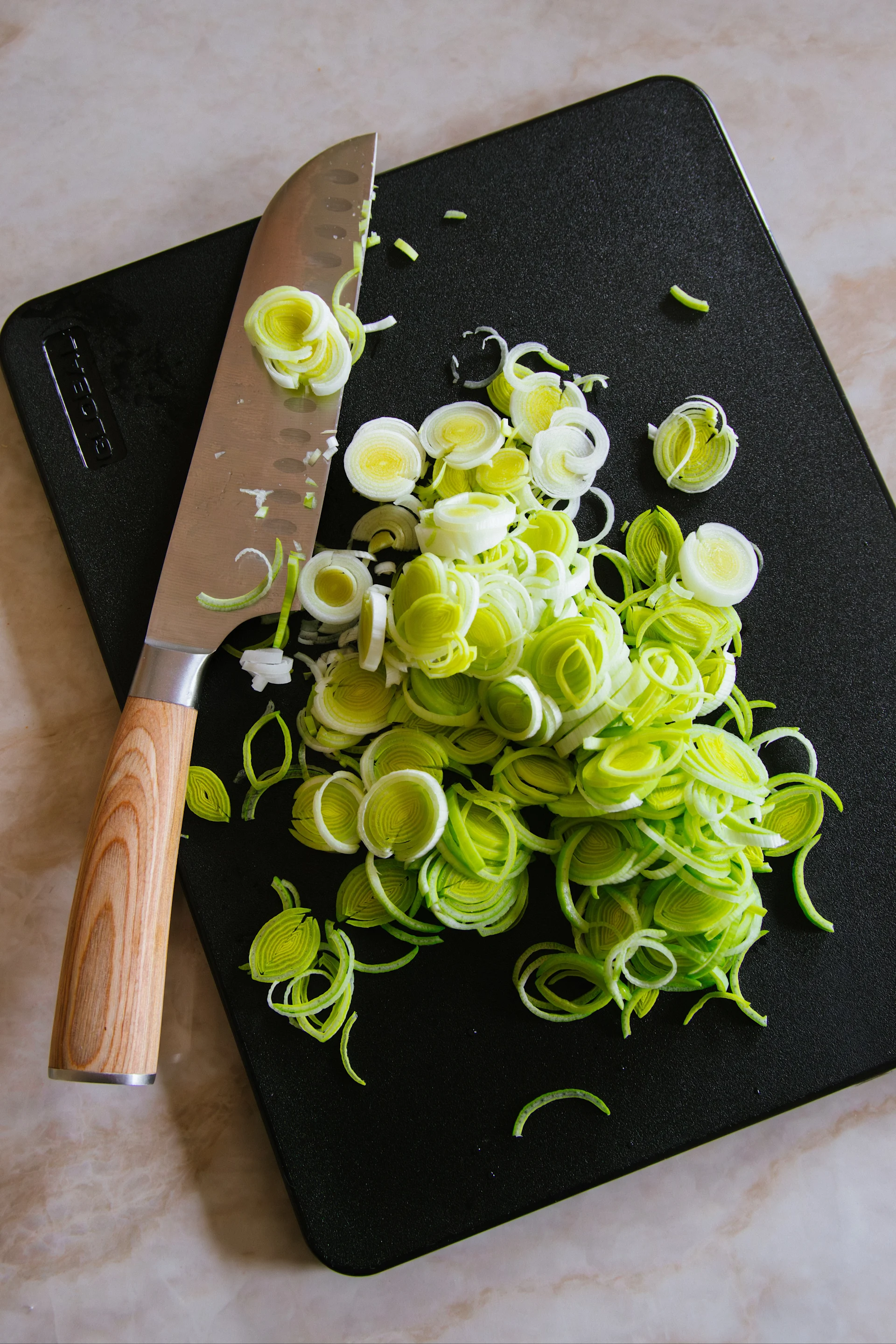 Skivad purjolök och en kniv på en svart skärbräda.