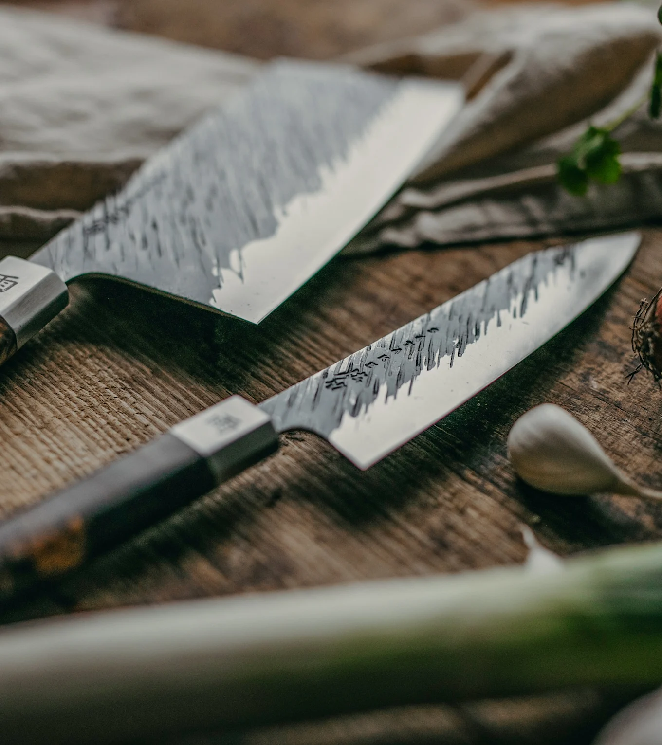 Två texturerade kockknivar med mörka handtag på en rustik träbräda med vitlök och salladslök.