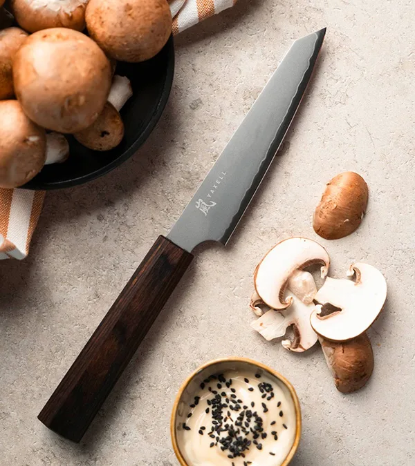 Kockkniv med mörkt blad och trähandtag, bredvid hela och skivade svampar och en skål sås.