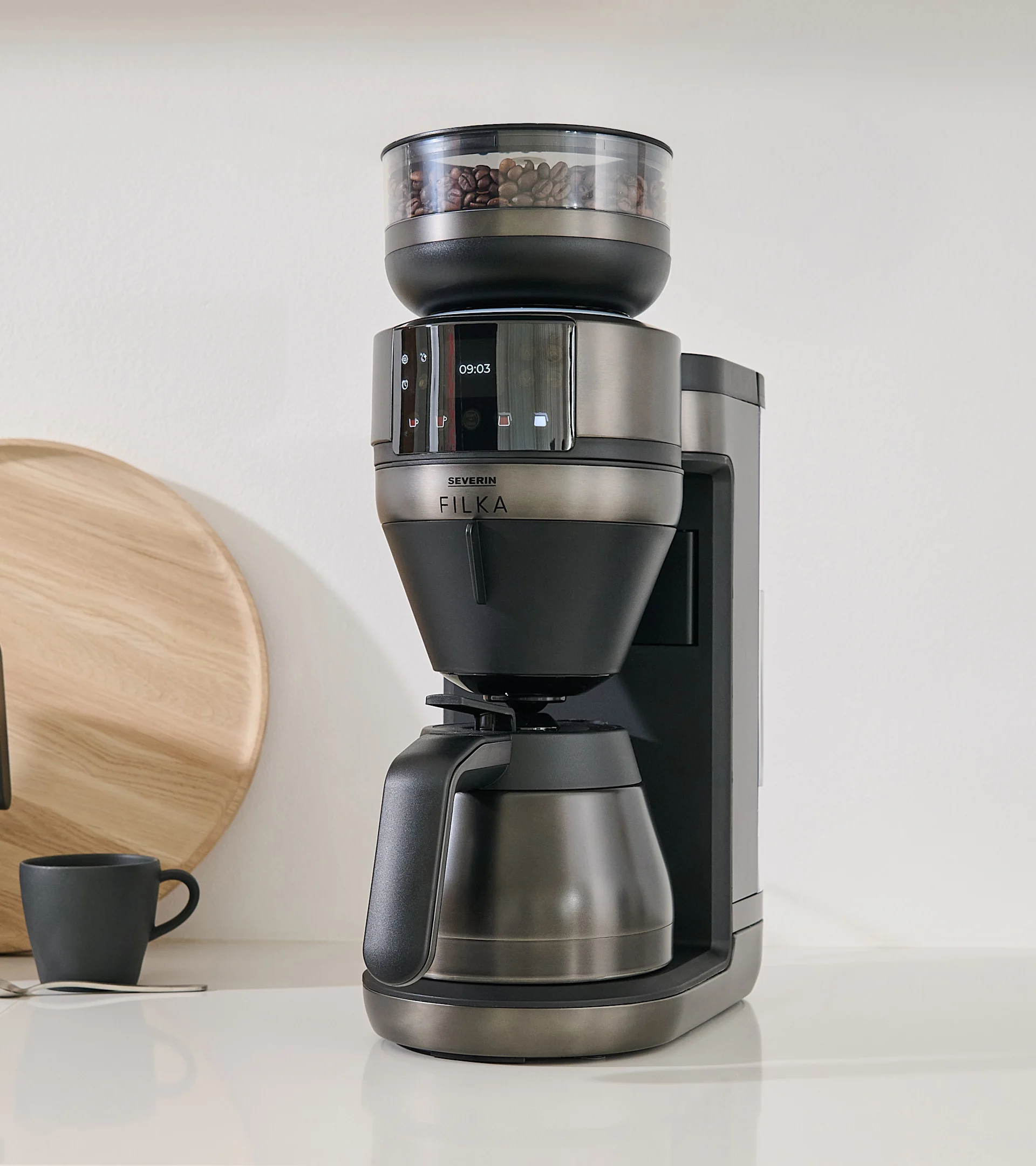 Mörkgrå och svart kaffemaskin med integrerad kvarn och synliga kaffebönor på en vit bänkskiva.