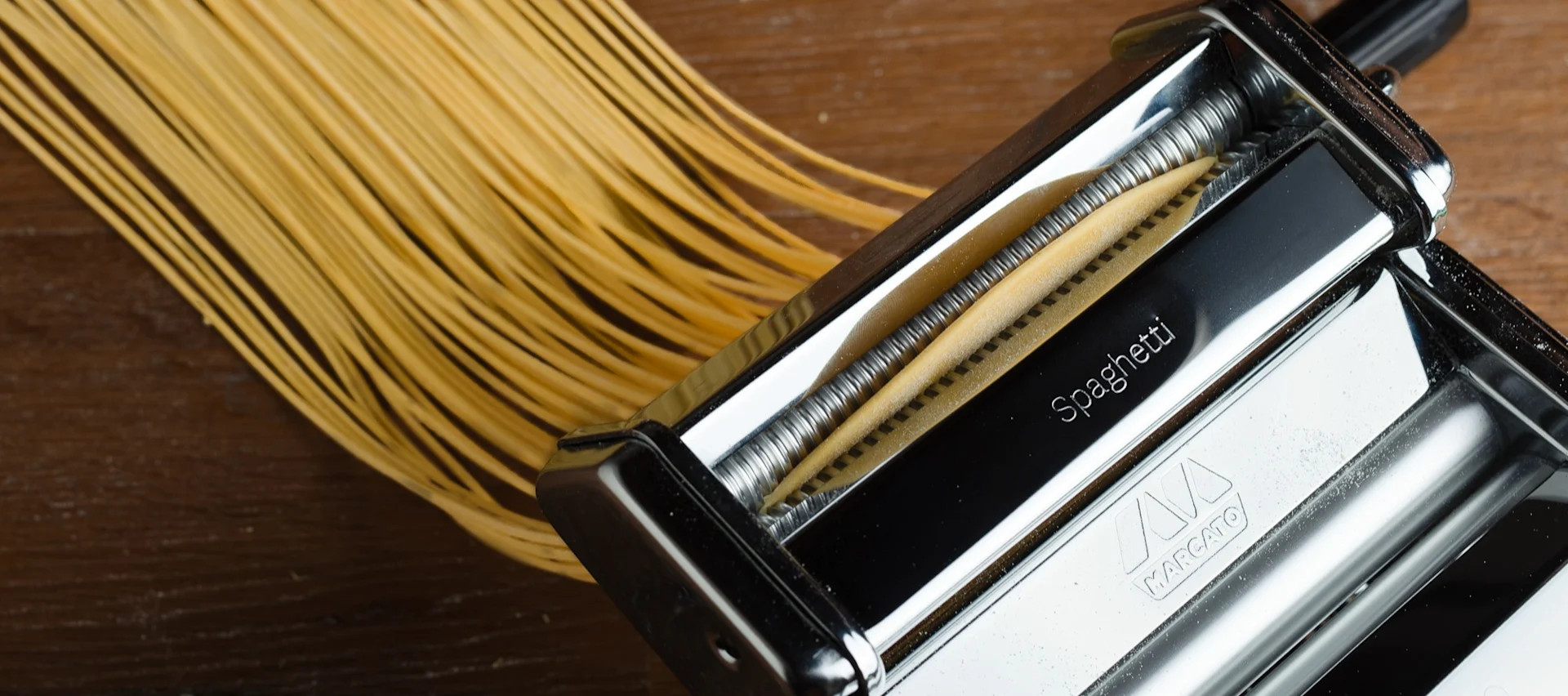 Färsk spaghetti extruderas från en pastamaskin ner på en träyta.