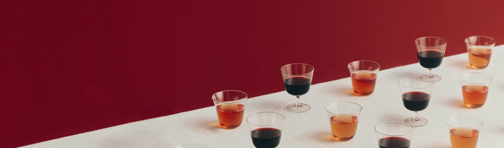 Olika glas med röda och bärnstensfärgade drycker på en vit yta med röd bakgrund.