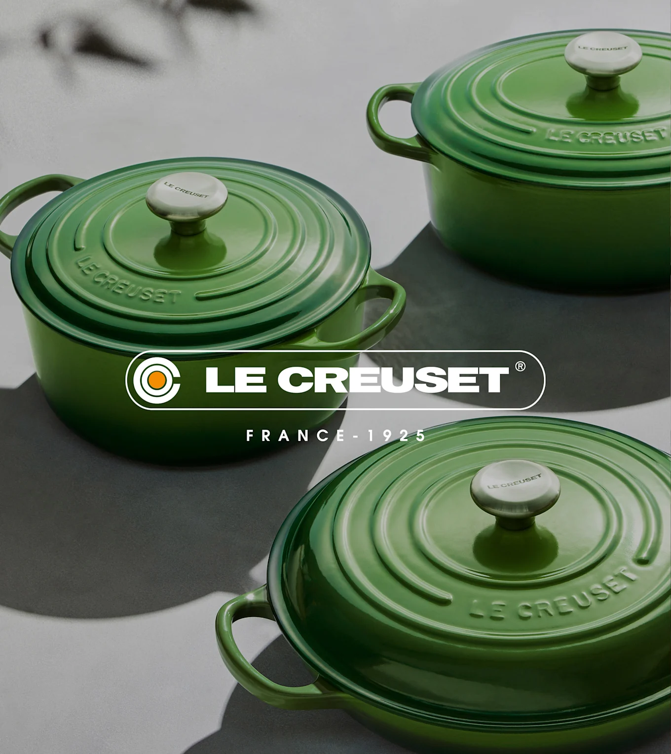 Tre gröna Le Creuset runda gjutjärnsgrytor med lock på en grå yta.