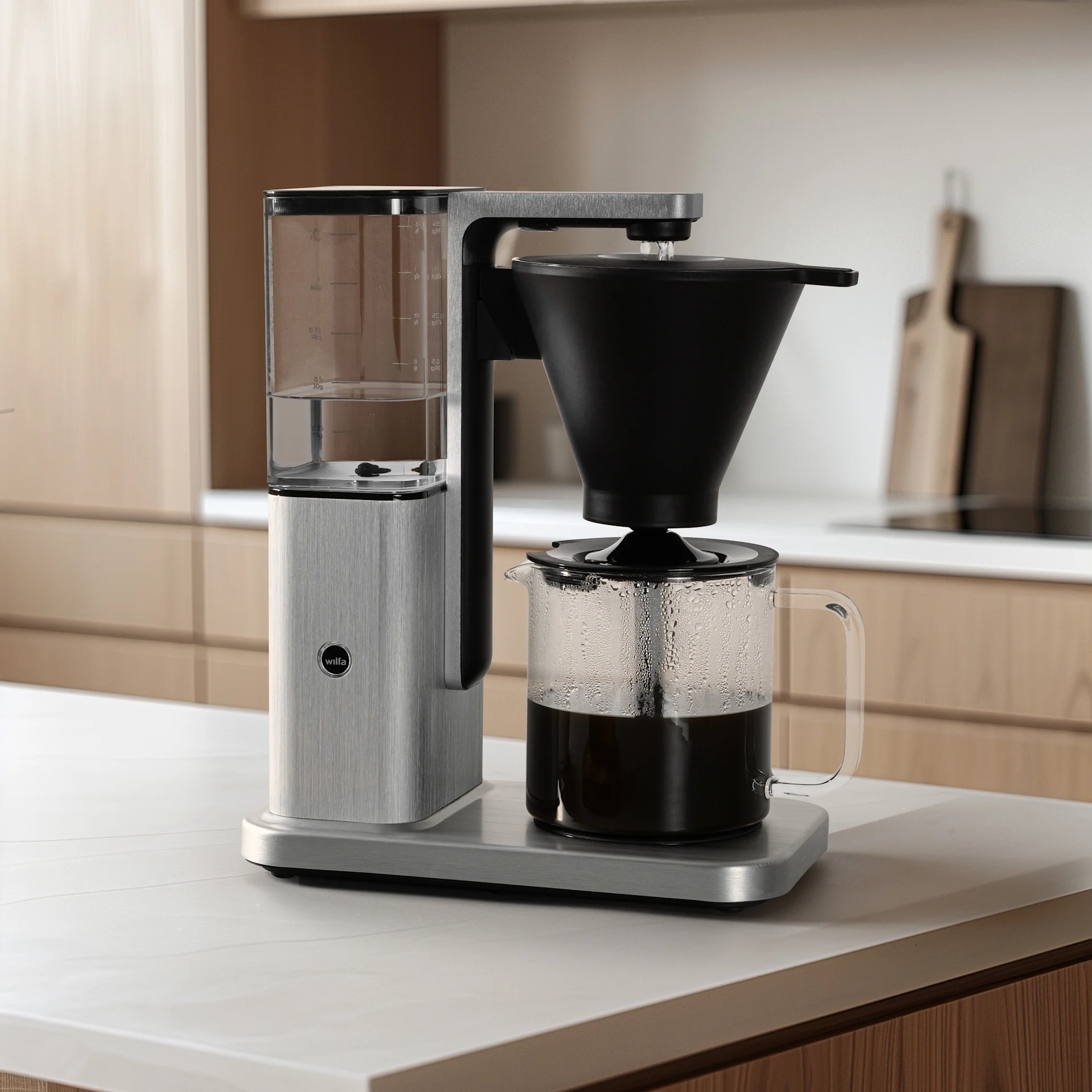 En modern kaffebryggare med borstad rostfri stålyta och en glaskanna full med varmt kaffe står på en köksbänk.