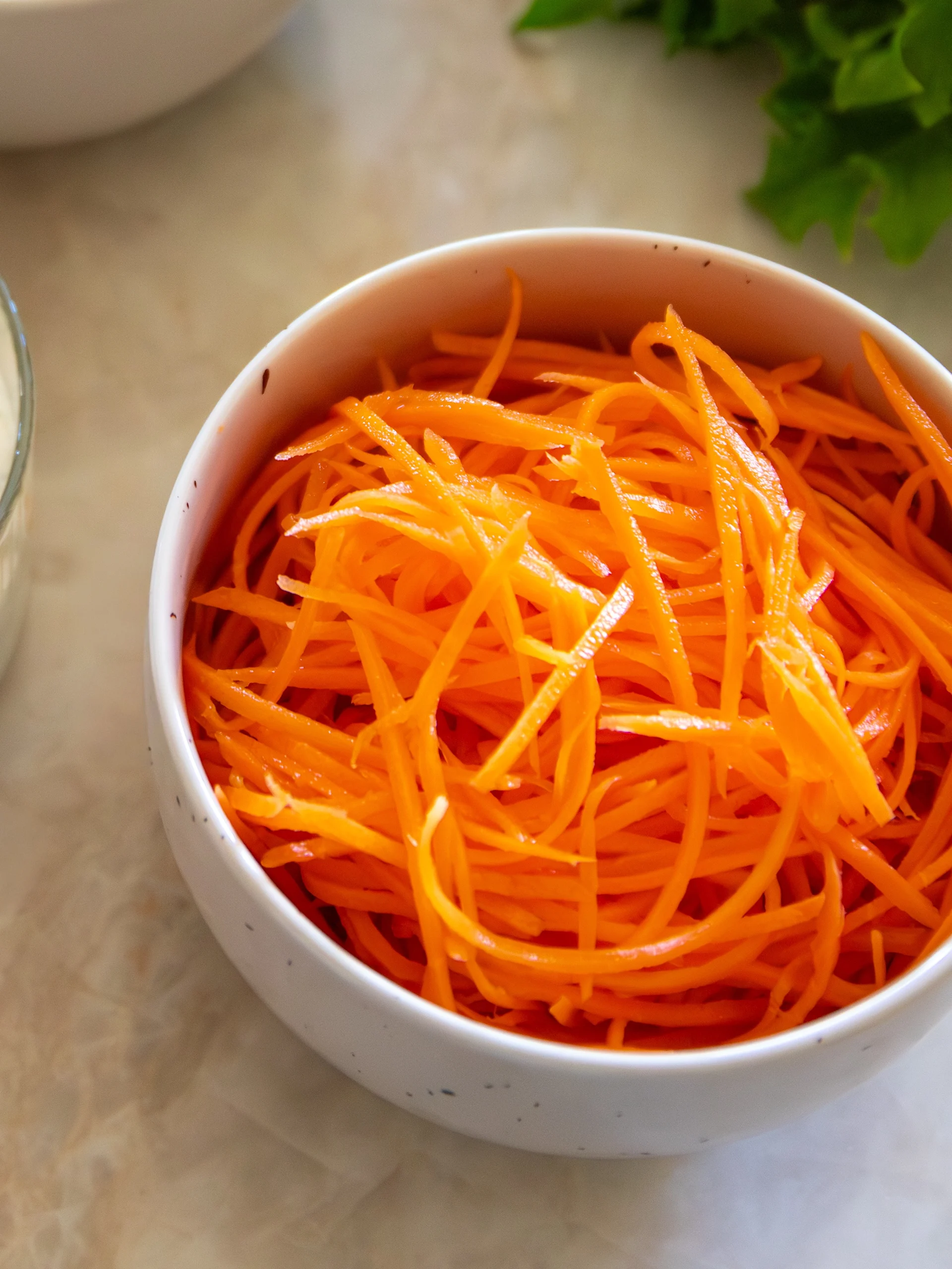 En vit skål fylld med livfullt orange strimlade morötter.