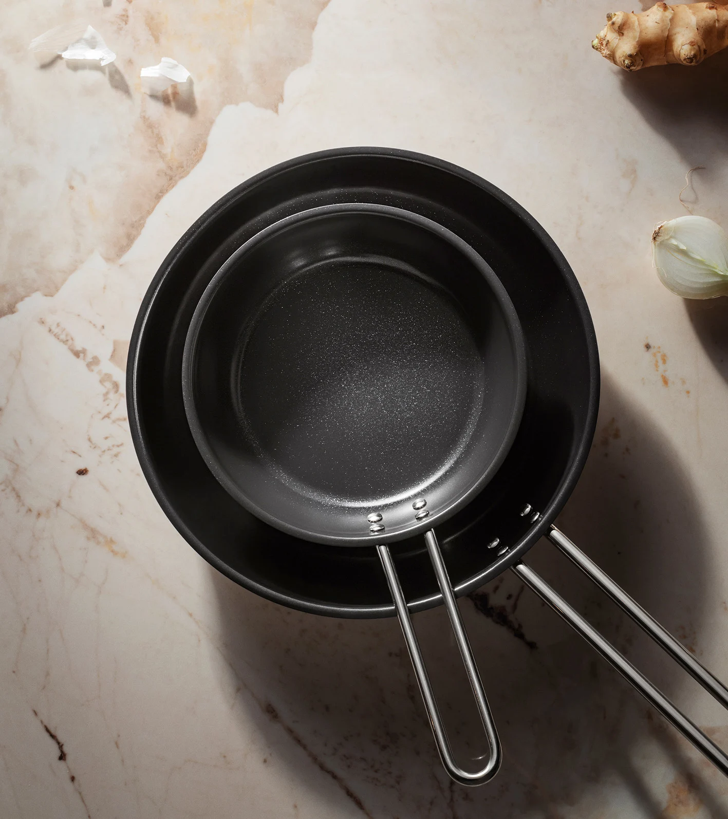 Två svarta non-stick stekpannor, en inuti den andra, på en marmoryta.