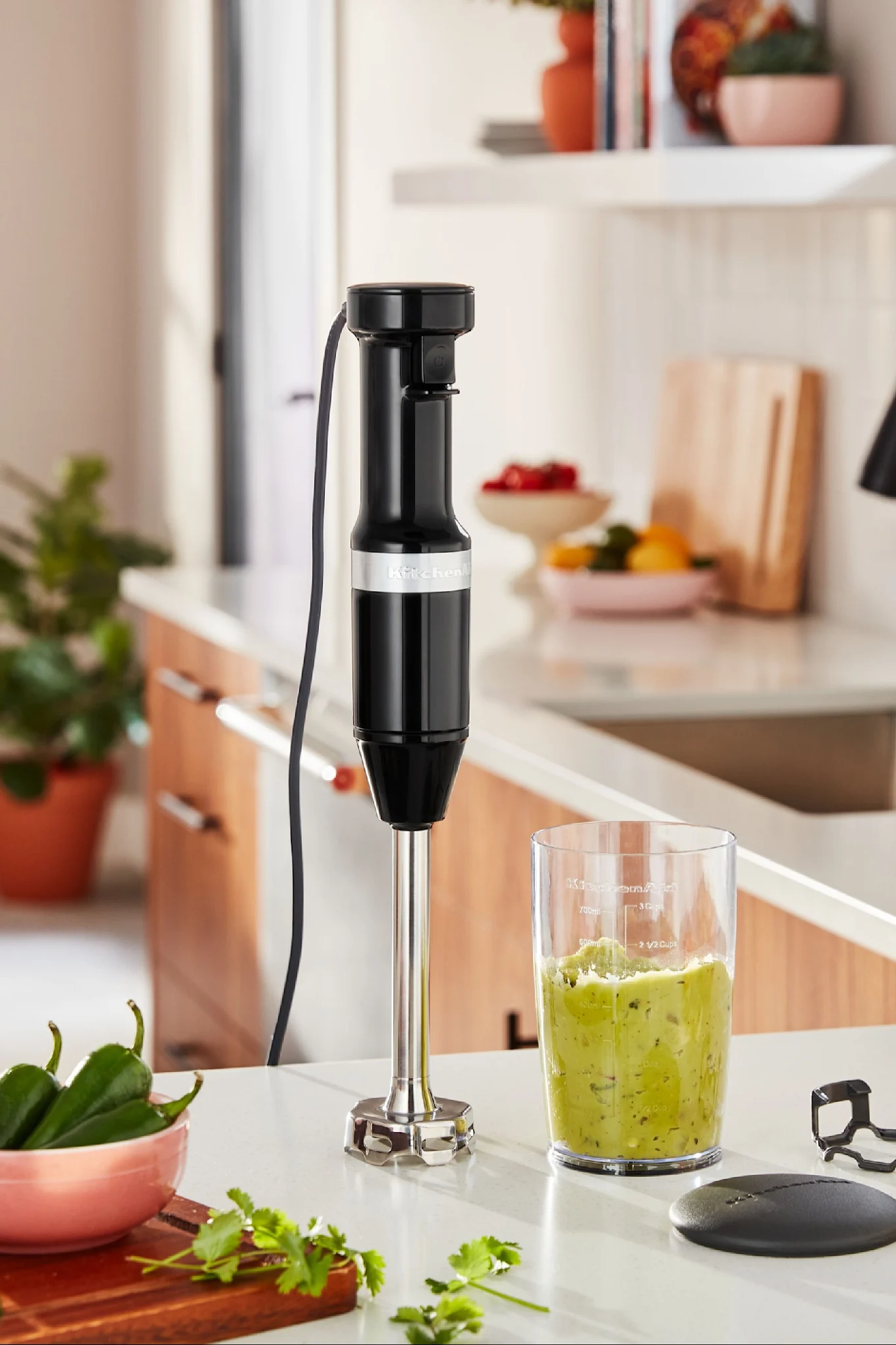 Stavmixern från KitchenAid står på en köksbänk med en smoothie bredvid sig.