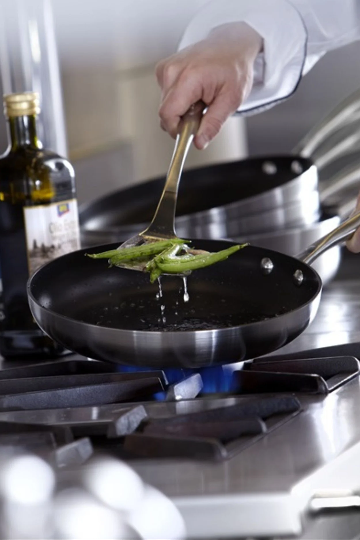 Någon öser gröna bönor ur en stekpanna med non stick-beläggning. 