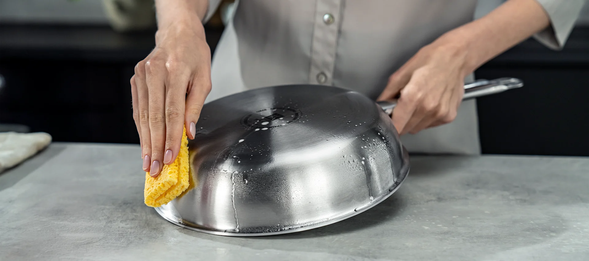 Hur rengör man en stekpanna i rostfritt stål? Här ser du någon rengöra botten på en rostfri stekpanna med en gul svamp. 