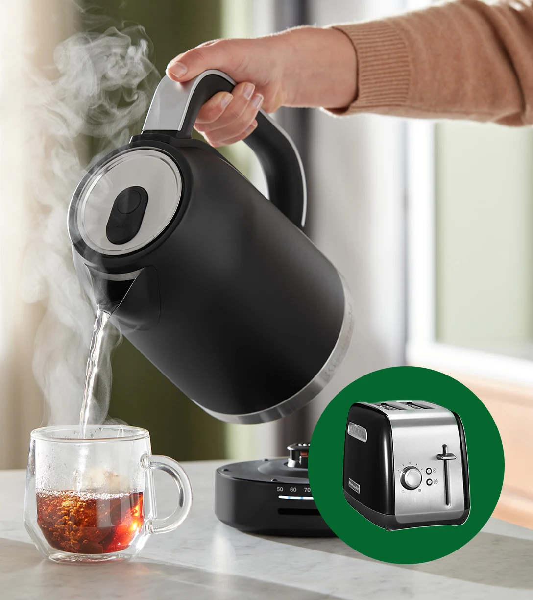 Hand häller ångande vatten från svart vattenkokare i klar temugg. Inbäddad: svart och silverfärgad brödrost.
