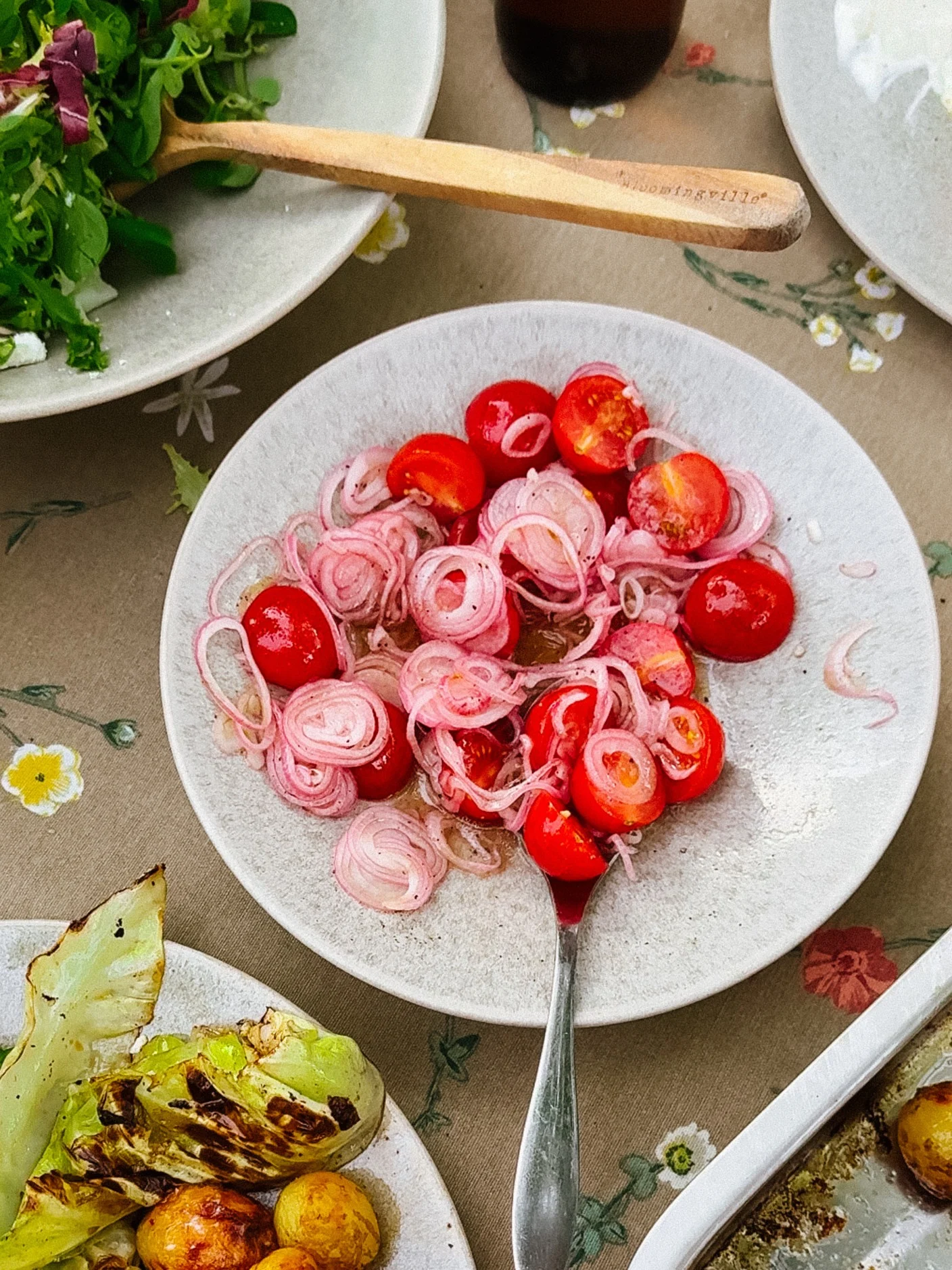 En tallrik med körsbärstomater och rödlök, del av en måltid med sallad och grillad kål.