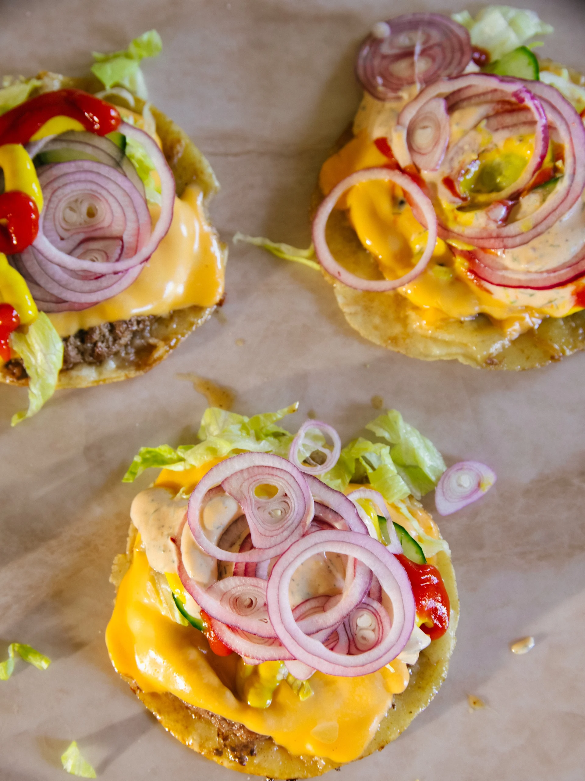 Tre öppna hamburgare med ost, sallad, rödlök, ketchup, senap och krämig sås.